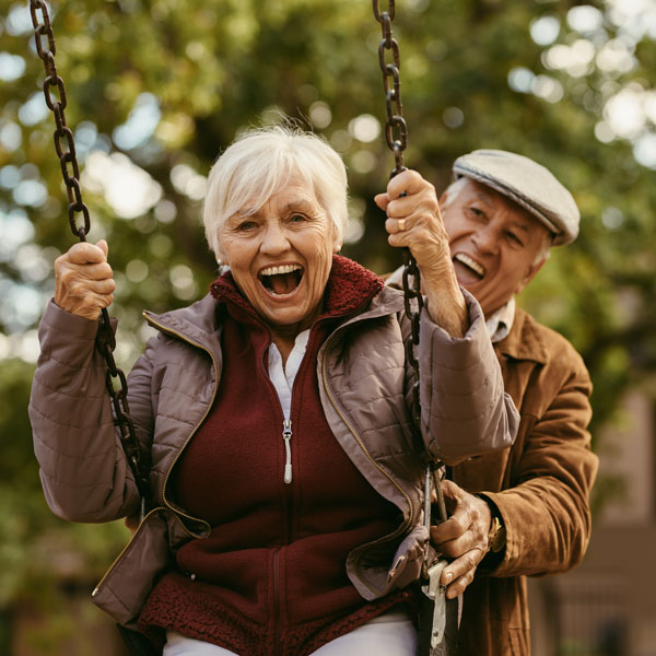 senior man and woman laughing using park swing