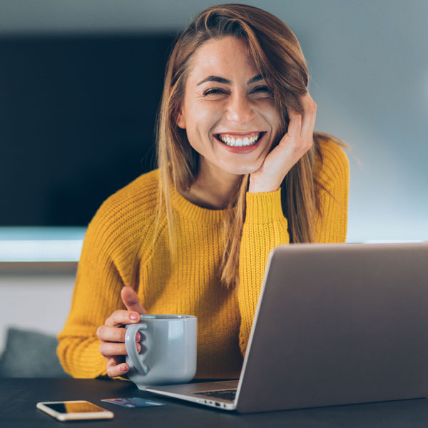 woman in yellow sweater smiling with coffee cup and laptop