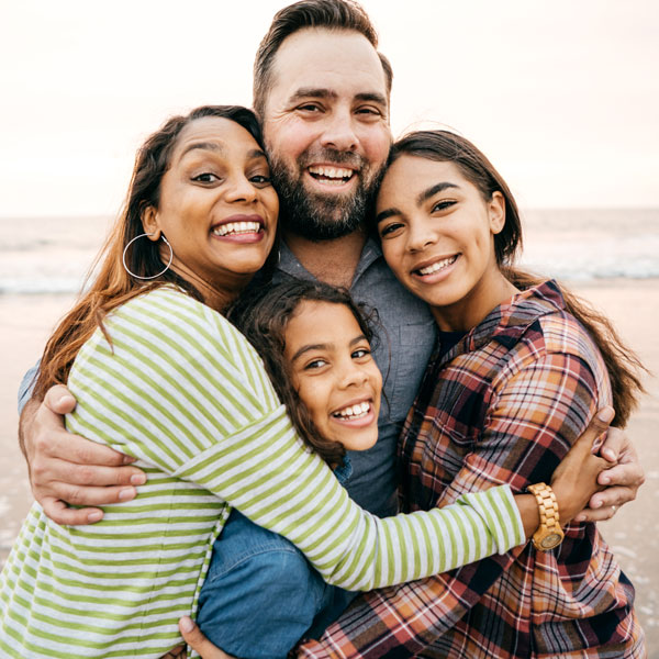 family with two teenage children smiling on beach